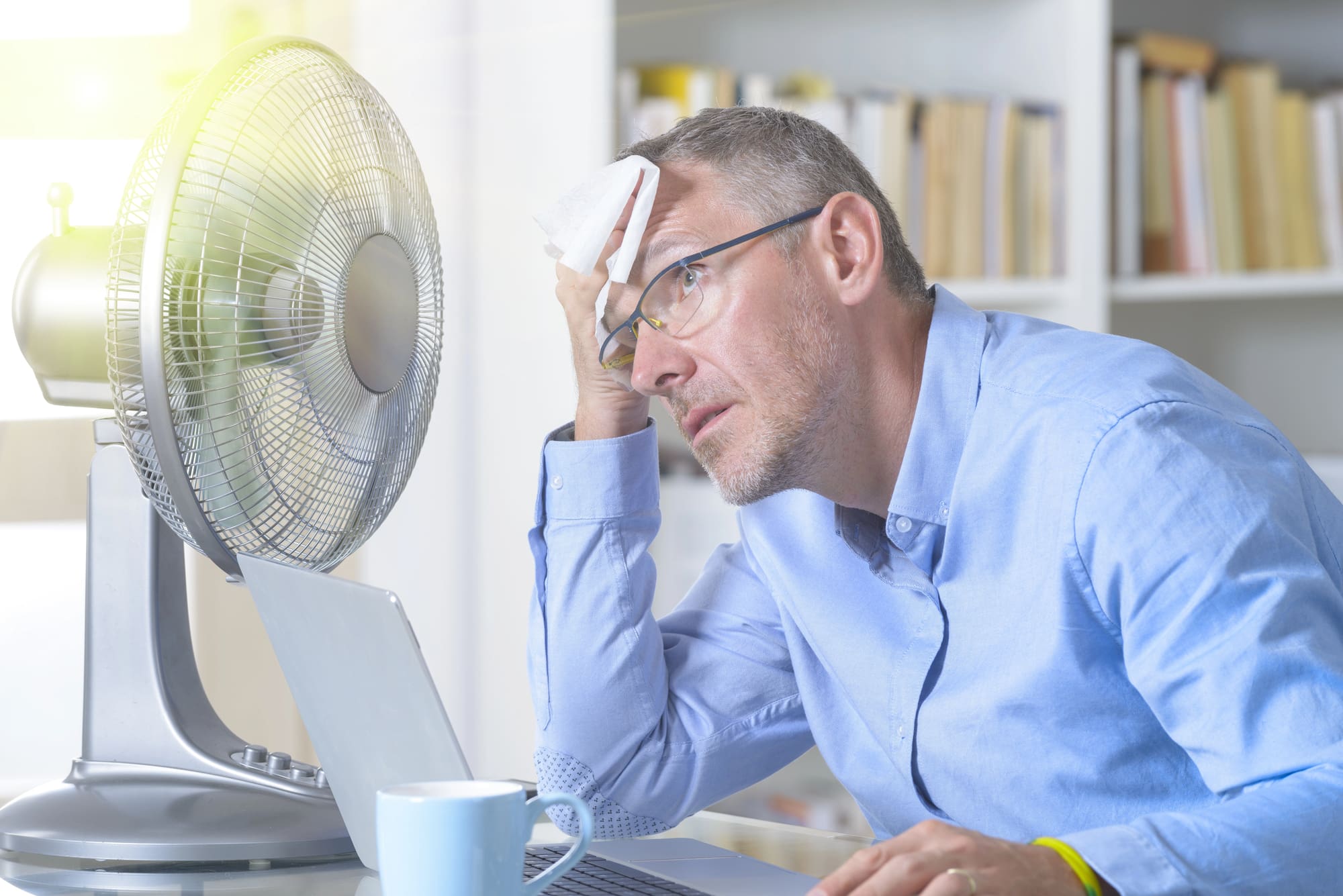 air conditioning system replacement Lynchburg hot Air conditioning system replacement Lynchburg needed as man cools himself with a desk fan in hot office.